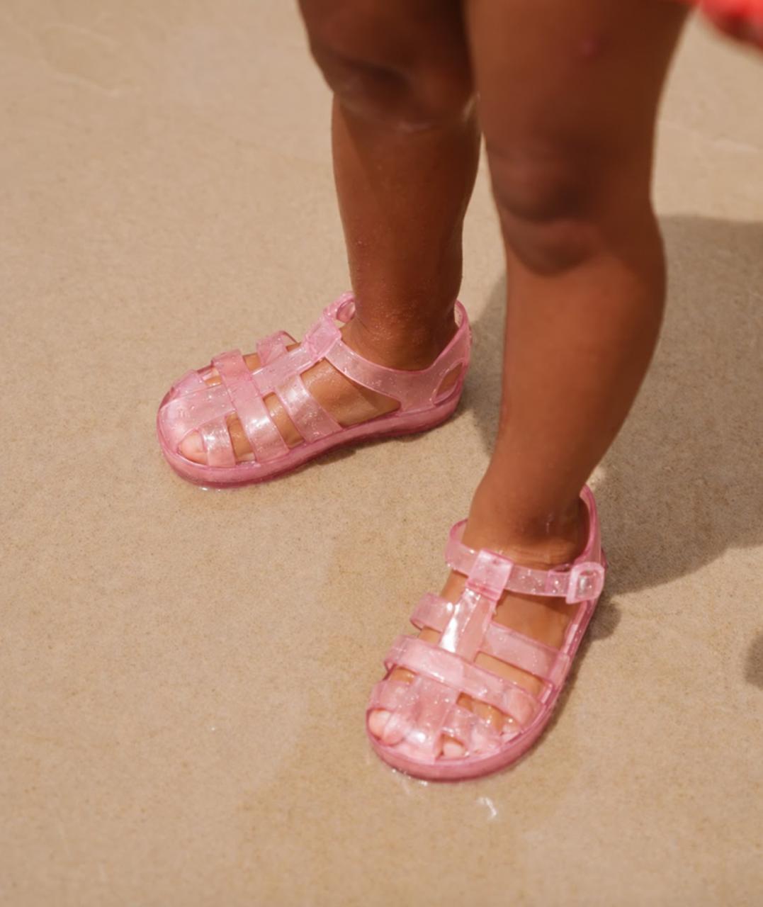 Child wearing pink glitter Frankie jelly sandals on the sand